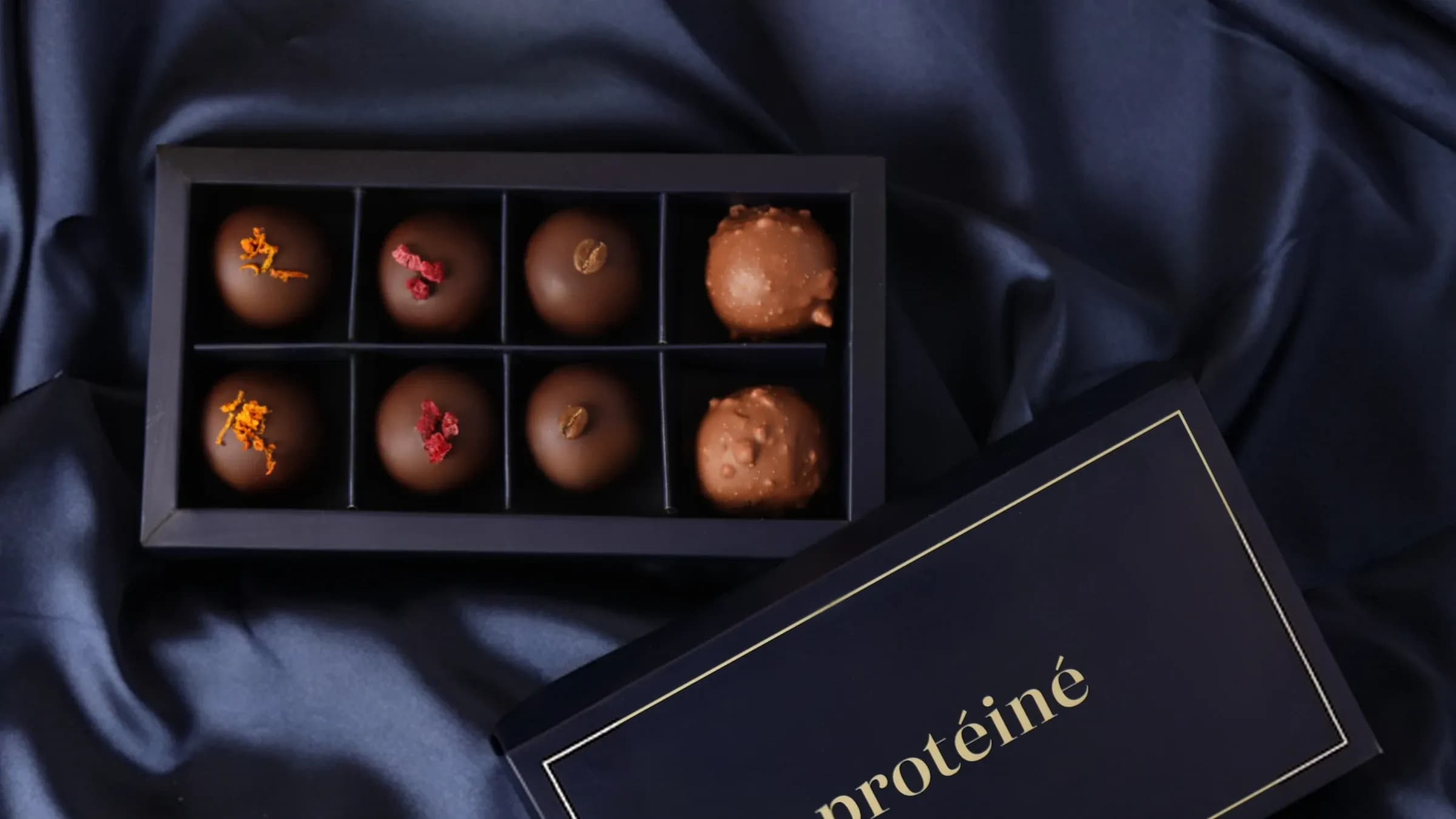 A box of eight, open on navy silk, its lid beside it.